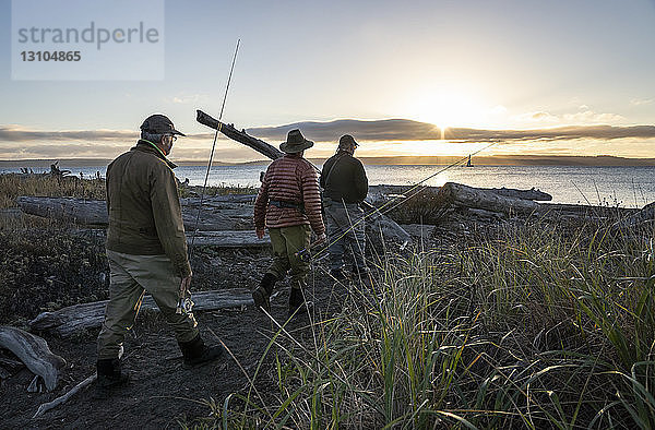 Zwei Fliegenfischer und ein Führer gehen bei Sonnenaufgang zu einem Salzwasserstrand  um an einem Strand an der Westküste der USA nach Cutthroat-Forellen und Lachsen zu fischen