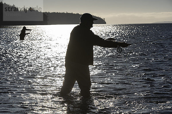 Die Silhouette von zwei Fliegenfischern  die im Salzwasser stehen  während sie im Nordwesten des Bundesstaates Washington im Fliegenfischen auf Meerforellen und Lachs fischen