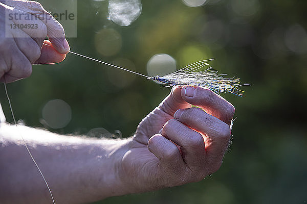 Nahaufnahme eines Fliegenfischers  der eine neue gefiederte Angelfliege an seine Schnur bindet  um sie im Salzwasser zu verwenden.
