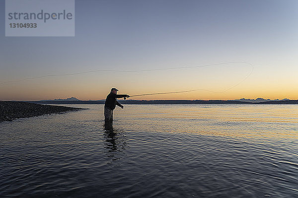 Die Silhouettenansicht eines Fliegenfischers  der an einem Strand an der Nordwestküste der USA von einem Salzwasserstrand aus nach Lachsen und Cutthroat-Forellen der Searun-Küste wirft.