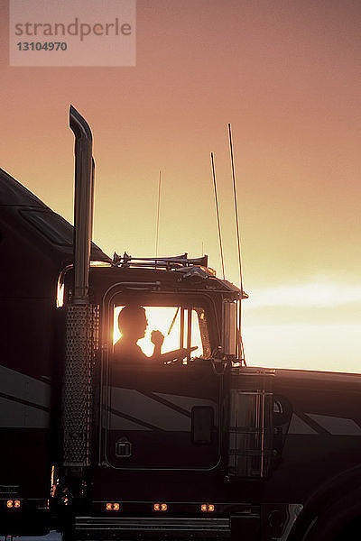 Die Silhouette eines Lkw-Fahrers auf seinem CB-Funkgerät im Führerhaus seines Lkw der Klasse 8.