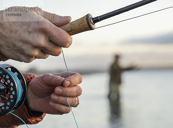 Nahaufnahme der Hände eines Fliegenfischers  der beim Angeln seine Fliegenrute und Schnur hält.