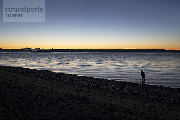 Ein Fliegenfischer macht sich bereit  bei Sonnenaufgang ins Salzwasser zu waten und an einem Strand an der Nordwestküste der USA mit der Fliege nach Cutthroat-Forellen und Lachsen zu fischen. USA
