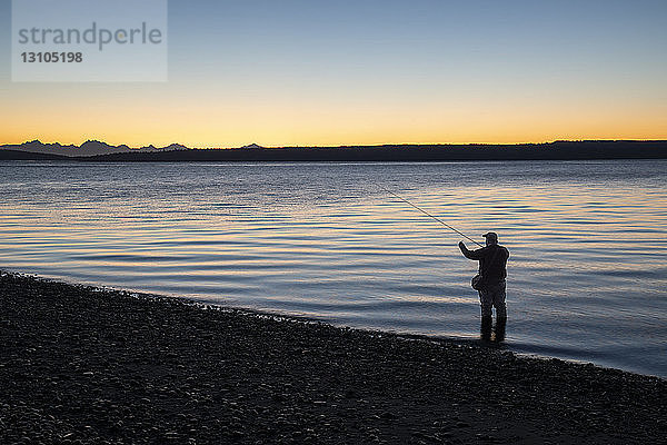 Ein Fliegenfischer macht sich bereit  bei Sonnenaufgang ins Salzwasser zu waten und an einem Strand an der Nordwestküste der USA mit der Fliege nach Cutthroat-Forellen und Lachsen zu fischen. USA