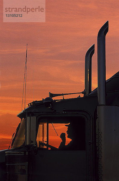 Die Silhouette eines Lkw-Fahrers auf seinem CB-Funkgerät im Führerhaus seiner Sattelzugmaschine der Klasse 8.