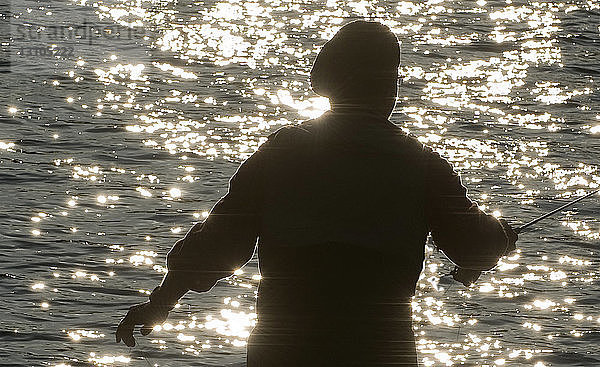 Silhouette eines Fliegenfischers  der in einem Fluss nach Forellen wirft