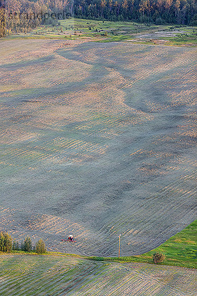 Blick vom Gipfel des Butte auf einen Traktor  der ein Feld bearbeitet  Süd-Zentral-Alaska; Palmer  Alaska  Vereinigte Staaten von Amerika