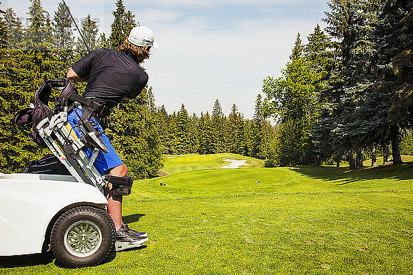 Ein körperlich behinderter Golfer  der einen Spezialrollstuhl benutzt  schlägt ab und schlägt einen Ball auf dem Fairway eines Golfplatzes; Edmonton  Alberta  Kanada