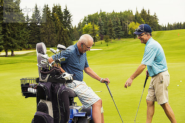 Ein nichtbehinderter Golfer unterstützt einen behinderten Golfer  der einen speziellen elektrischen Golfrollstuhl benutzt  während sie zusammen auf einem Golfplatz den besten Ball spielen; Edmonton  Alberta  Kanada