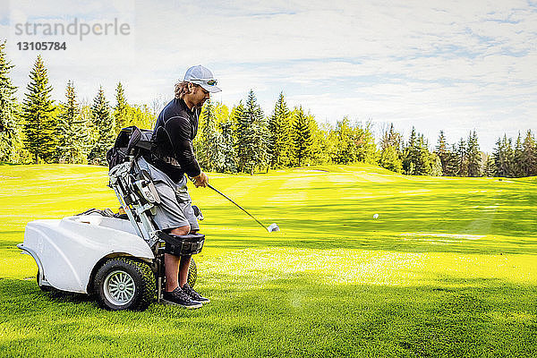 Ein körperlich behinderter Golfer  der einen Ball auf einem Golfplatz schlägt und einen speziellen motorisierten Hydraulikrollstuhl zur Golfunterstützung benutzt; Edmonton  Alberta  Kanada