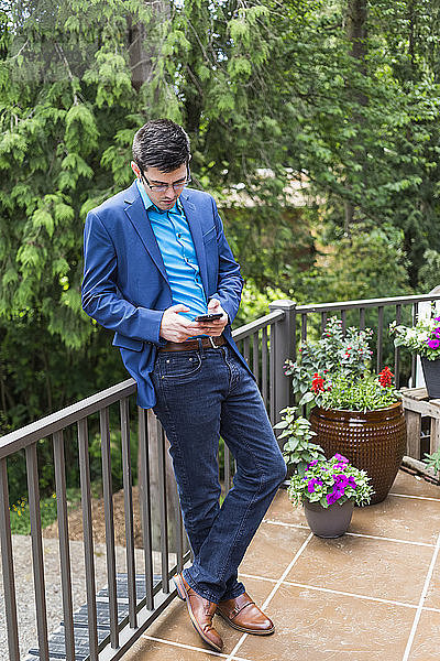 Ein junger Mann benutzt sein Smartphone  während er auf einer Veranda steht; Bothell  Washington  Vereinigte Staaten von Amerika