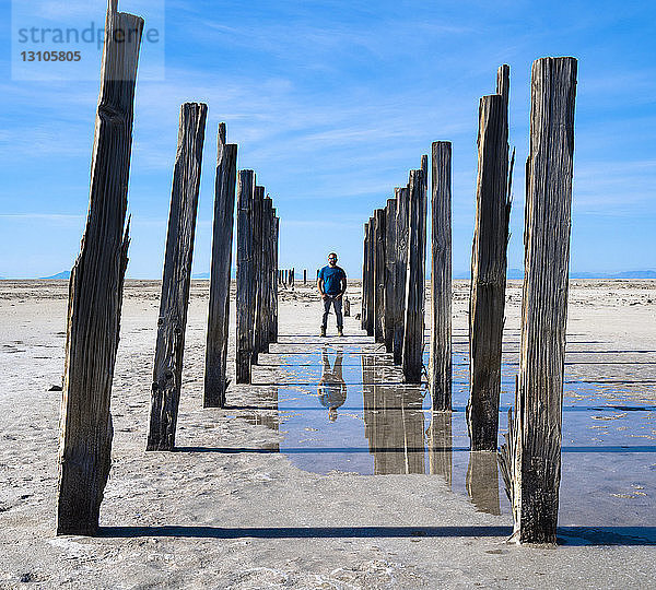 Spiegelung eines Mannes im flachen Wasser  der in einer kargen Landschaft steht  mit Holzpfählen in einer Reihe auf beiden Seiten von ihm  Great Salt Lake; Utah  Vereinigte Staaten von Amerika