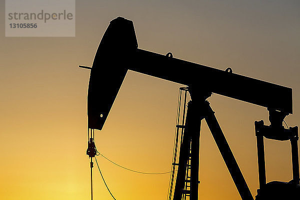 Silhouette eines Pumpjacks bei Sonnenaufgang mit einem glühend warmen Himmel  westlich von Airdrie; Alberta  Kanada