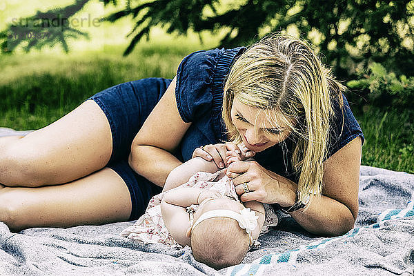 Eine junge Mutter spielt mit ihrem Baby auf einer Decke in einem Stadtpark an einem warmen Sommertag; Edmonton  Alberta  Kanada