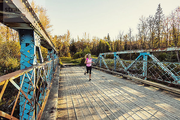 Eine attraktive Frau mittleren Alters läuft über eine Brücke  während sie an einem schönen warmen Herbstabend in einem Stadtpark trainiert; Edmonton  Alberta  Kanada
