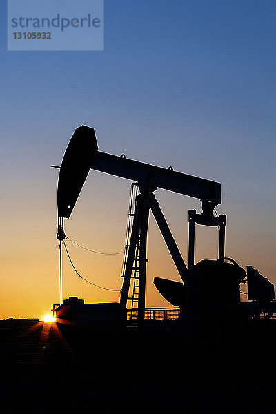 Silhouette eines Pumpjacks bei Sonnenaufgang mit orangefarbenem Sonnenschliff; Acme  Alberta  Kanada