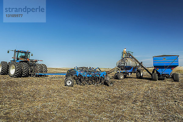 Landwirt steht auf einem Trichter  der mit einem anderen Trichter gefüllt wird  auf einem Feld mit blauem Himmel; Beiseker  Alberta  Kanada