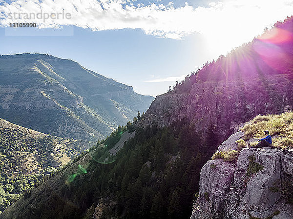 Ein Mann sitzt auf einem Bergrücken und blickt auf die Berge und Täler unter ihm  während das Sonnenlicht auf den Berghang fällt; Logan  Utah  Vereinigte Staaten von Amerika