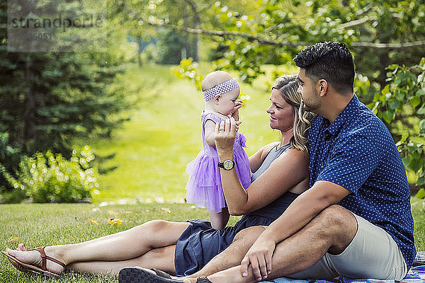 Ein gemischtrassiges Ehepaar entspannt sich an einem warmen Herbstnachmittag zusammen mit seinem kleinen Mädchen auf einer Decke in einem Park; Edmonton  Alberta  Kanada