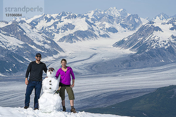 Ein Paar genießt die Sehenswürdigkeiten und die Landschaft des Kluane National Park and Reserve an einem sonnigen Tag  nachdem es einen Schneemann gebaut hat; Haines Junction  Yukon  Kanada
