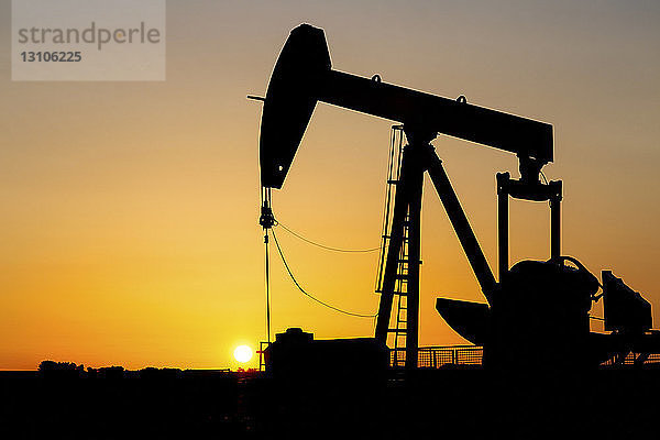 Silhouette eines Pumpjacks bei Sonnenaufgang mit einem glühend warmen Himmel  westlich von Airdrie; Alberta  Kanada