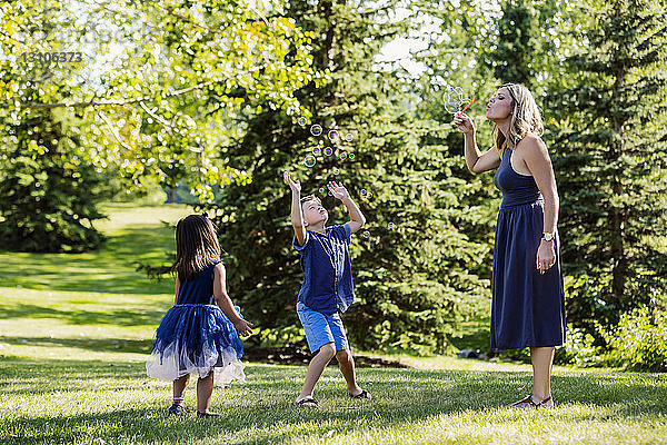 Eine Mutter bläst Seifenblasen für ihre Kinder während eines Familienausflugs in einem Park an einem warmen Herbsttag; Edmonton  Alberta  Kanada