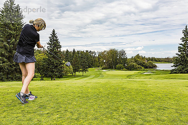 Eine Golferin schlägt einen Golfball gekonnt über das grüne Gras eines Golfplatzes  während der Ball in der Luft ist; Edmonton  Alberta  Kanada