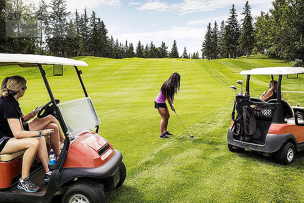 Eine Gruppe von Golferinnen schaut von ihren Golfwagen aus zu  während ihre Teamkollegin ihren Schlag aus dem Rough auf einem Golfplatz an einem warmen Sommertag plant; Edmonton  Alberta  Kanada