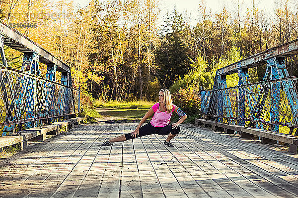 Eine attraktive Frau mittleren Alters macht eine Pause  um ihre Beine auf einer Brücke auszustrecken  während sie an einem schönen warmen Herbstabend in einem Stadtpark läuft; Edmonton  Alberta  Kanada