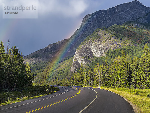 Straße durch die zerklüfteten kanadischen Rocky Mountains mit einem Regenbogen unter den Gewitterwolken; Alberta  Kanada