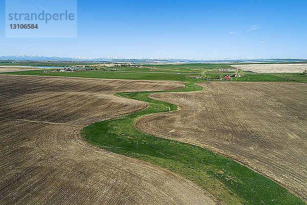 Luftaufnahme eines grünen Grabenstücks inmitten eines gesäten Feldes mit Bergen und blauem Himmel  westlich von High River; Alberta  Kanada