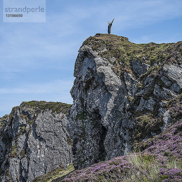 Ein Mann steht mit erhobenen Armen am Rand einer felsigen Klippe und schaut hinaus; Carrick  Grafschaft Donegal  Irland