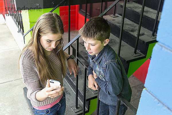 Ein Mädchen und ein Junge im Teenageralter stehen zusammen und schauen auf ein Smartphone; Salmon Arm  British Columbia  Kanada