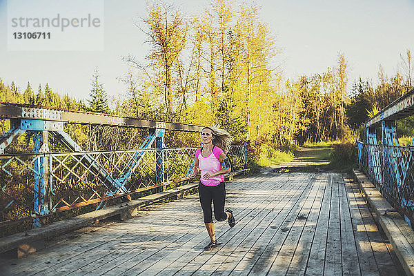Eine attraktive Frau mittleren Alters läuft über eine Brücke  während sie trainiert und Musik auf ihrem Smartphone hört  an einem schönen warmen Herbstabend in einem Stadtpark; Edmonton  Alberta  Kanada