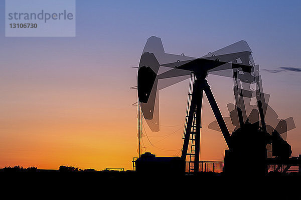 Mehrfachbelichtung einer Pumpjack-Silhouette bei Sonnenaufgang vor einem glühend warmen Himmel  westlich von Airdrie; Alberta  Kanada