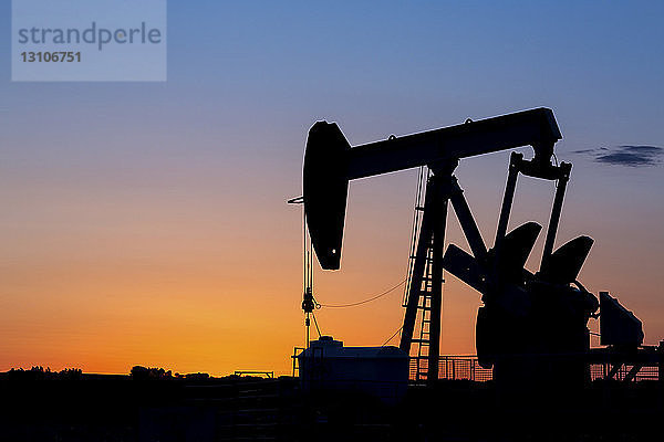 Silhouette eines Pumpjacks bei Sonnenaufgang mit einem glühend warmen Himmel  westlich von Airdrie; Alberta  Kanada