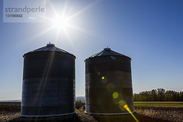 Silhouette von zwei großen Getreidesilos aus Metall in einem Feld mit Sonnenaufgang und blauem Himmel; Rockyford  Alberta  Kanada