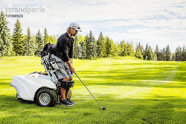 Ein körperlich behinderter Golfer  der einen Spezialrollstuhl benutzt  richtet seinen Driver auf dem Golfgrün auf den Ball aus; Edmonton  Alberta  Kanada