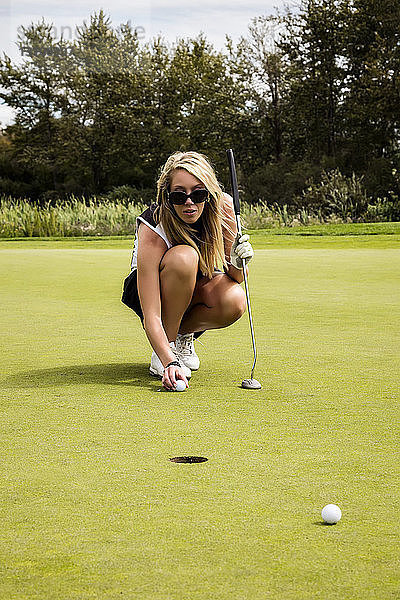 Eine attraktive Golferin hockt sich mit ihrem Golfball hin und richtet ihren Schlag aus  bevor sie einen kurzen Putt macht; Edmonton  Alberta  Kanada