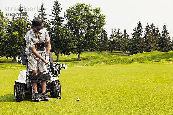 Ein körperlich behinderter Golfer  der einen Ball auf ein Golfgrün schlägt und einen speziellen motorisierten Hydraulikrollstuhl zur Golfunterstützung benutzt; Edmonton  Alberta  Kanada