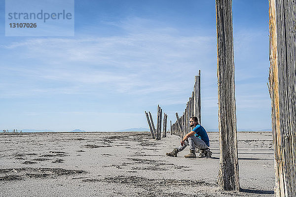 Ein Mann sitzt auf einem Baumstumpf auf einer kargen Fläche und schaut unter einem blauen Himmel mit Wolken hervor  Great Salt Lake; Utah  Vereinigte Staaten von Amerika