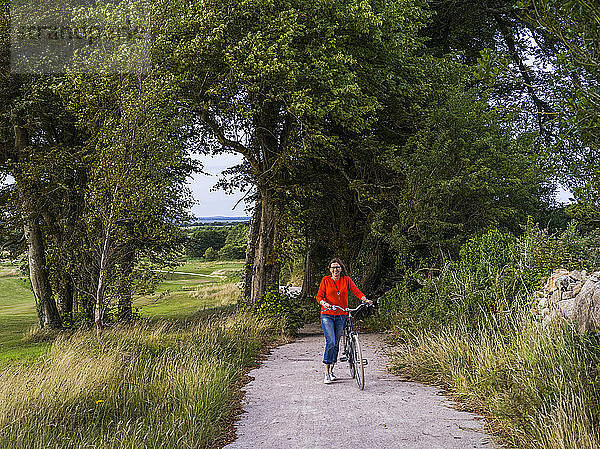 Eine Frau  die mit ihrem Fahrrad eine Straße beim Gleno Abbey Hotel und Golfplatz entlang fährt; County Galway  Irland