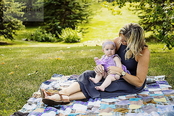 Eine Mutter und ihre kleine Tochter sitzen auf einer Picknickdecke und verbringen viel Zeit miteinander  während sie einen Familienausflug in einem Stadtpark an einem warmen Herbstnachmittag genießen; Edmonton  Alberta  Kanada