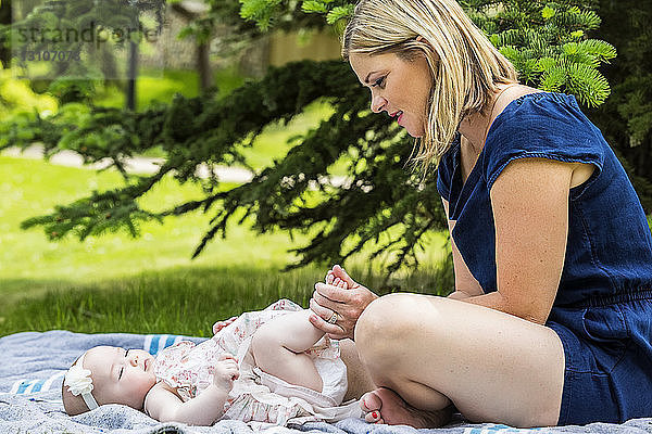 Eine junge Mutter spielt mit ihrem Baby auf einer Decke in einem Stadtpark an einem warmen Sommertag; Edmonton  Alberta  Kanada