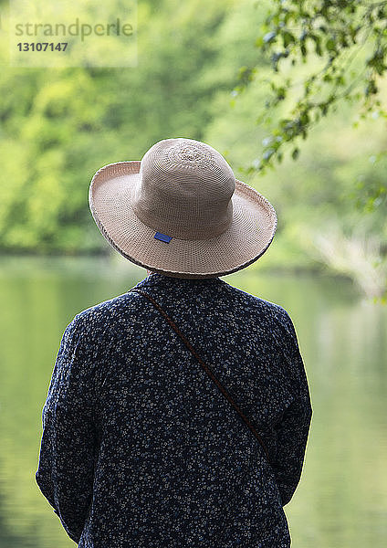 Eine Frau mit einem Hut mit Krempe schaut auf einen ruhigen See hinaus; Northumberland  England