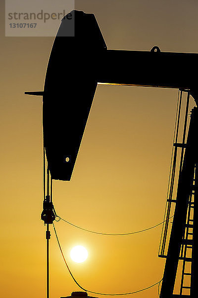 Silhouette eines Pumpjacks bei Sonnenaufgang mit einem glühend warmen Himmel  westlich von Airdrie; Alberta  Kanada