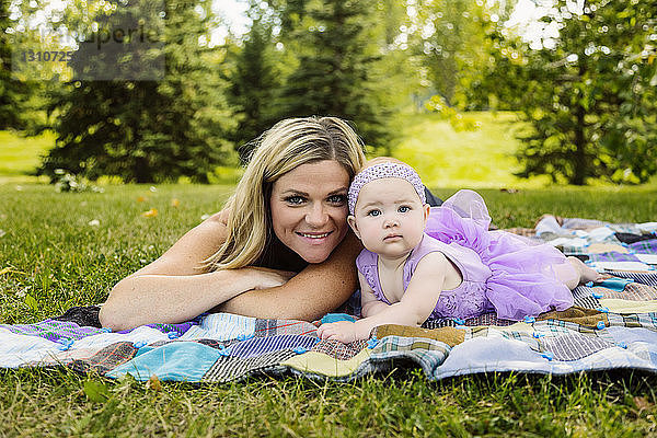 Eine Mutter und ihre kleine Tochter liegen auf einer Picknickdecke und posieren für die Kamera  während sie einen Familienausflug in einem Stadtpark an einem warmen Herbstnachmittag genießen; Edmonton  Alberta  Kanada
