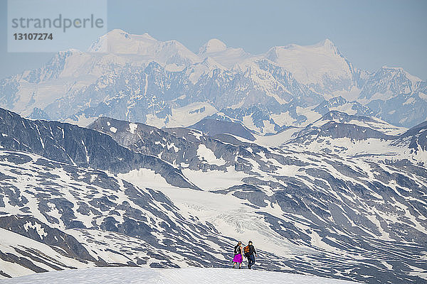 Paar  das auf einem Berggipfel spazieren geht  während sich in der Ferne die massiven Berge des Kluane National Park and Reserve abzeichnen; Haines Junction  Yukon  Kanada