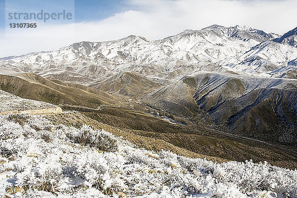 Ein Wüstental ist mit einer frischen Schneeschicht bedeckt. Die Szene wurde von einem Bergrücken mit Bergen in der Ferne fotografiert; Potrerillos  Mendoza  Argentinien