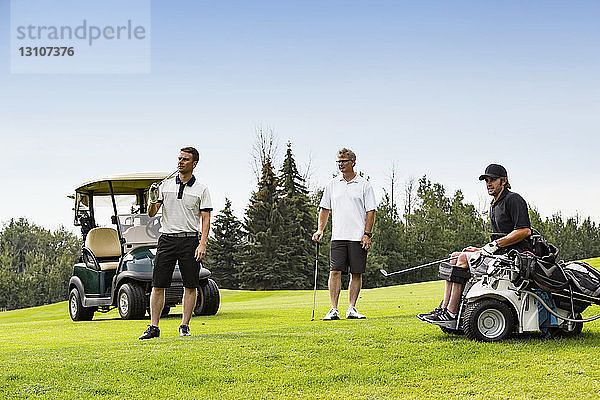 Eine Gruppe von Golfern  von denen einer mit einer Mobilitätshilfe behindert ist  beobachtet einen langen Abschlag auf dem Fairway; Edmonton  Alberta  Kanada